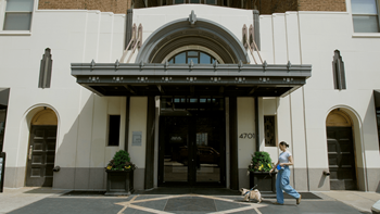 A woman walking her dog in front of a building with the number 4701 on it.